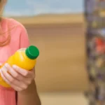 Femme décryptant l'étiquette d'un bouteille de jus pour vérifier la teneur en sucres cachés et ajoutés
